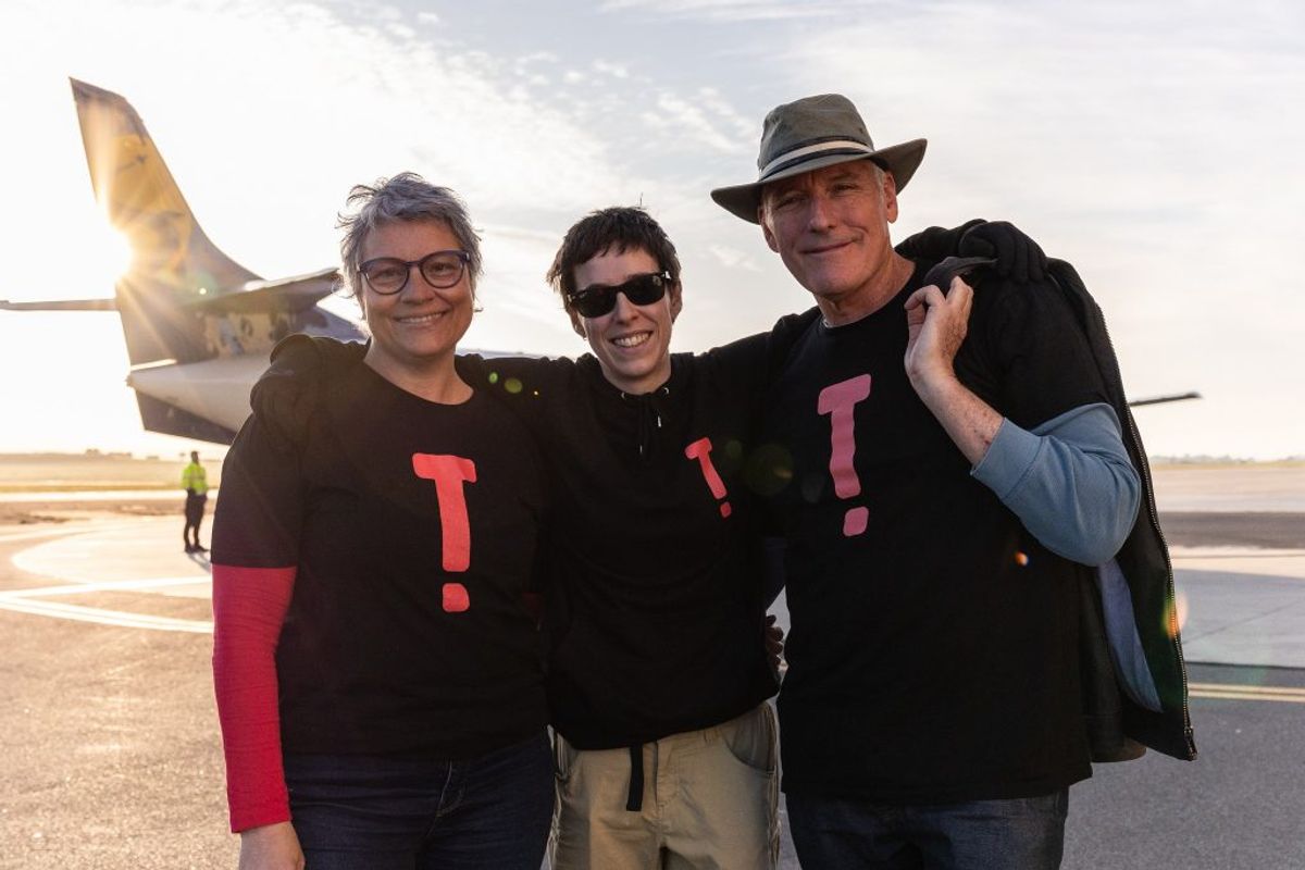 Three people stand smiling at us, there's a plane and airfield behind them, it's also sunrise and these people all wear Terrapin branded t-shirts