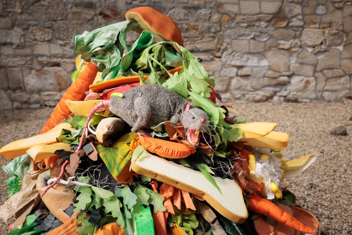 A pretend compost heap made of fabric and foam sits on e yellowy stone ground in front of a sandstone backdrop.