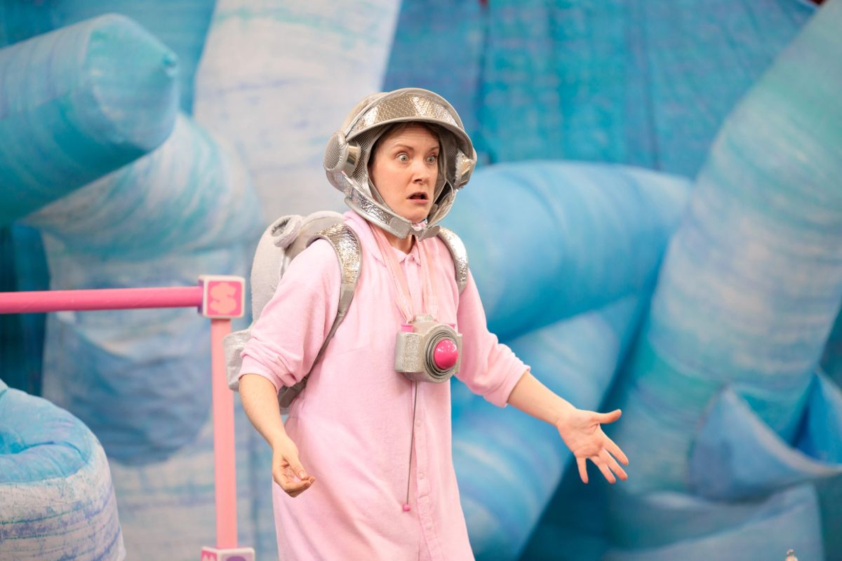 Jem as Baby in Space Neighbours on Uranus. Dressed in a pink onesie, silver space helmet and toy camera, she freezes in alarm as giant blue icebergs deflate behind her.