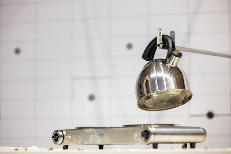 We see a variety of breakfast paraphernalia on a table, here we see a kettle and a hotplate operated by a long pole from a wall off in the distance.