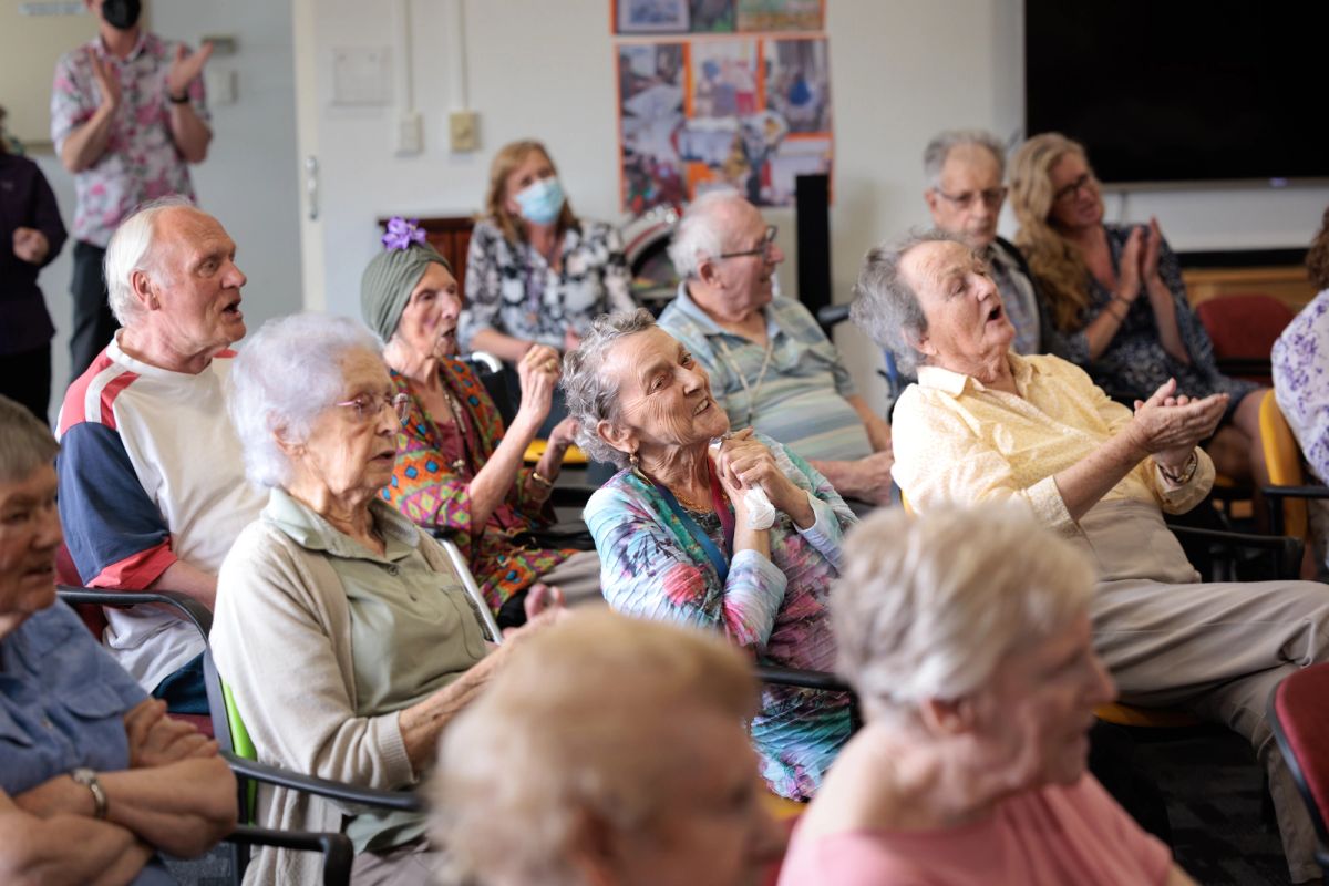 A group of elderly people sit in chairs looking towards the right hand side of the image, what the viewer doesn't see is the stage their all looking at