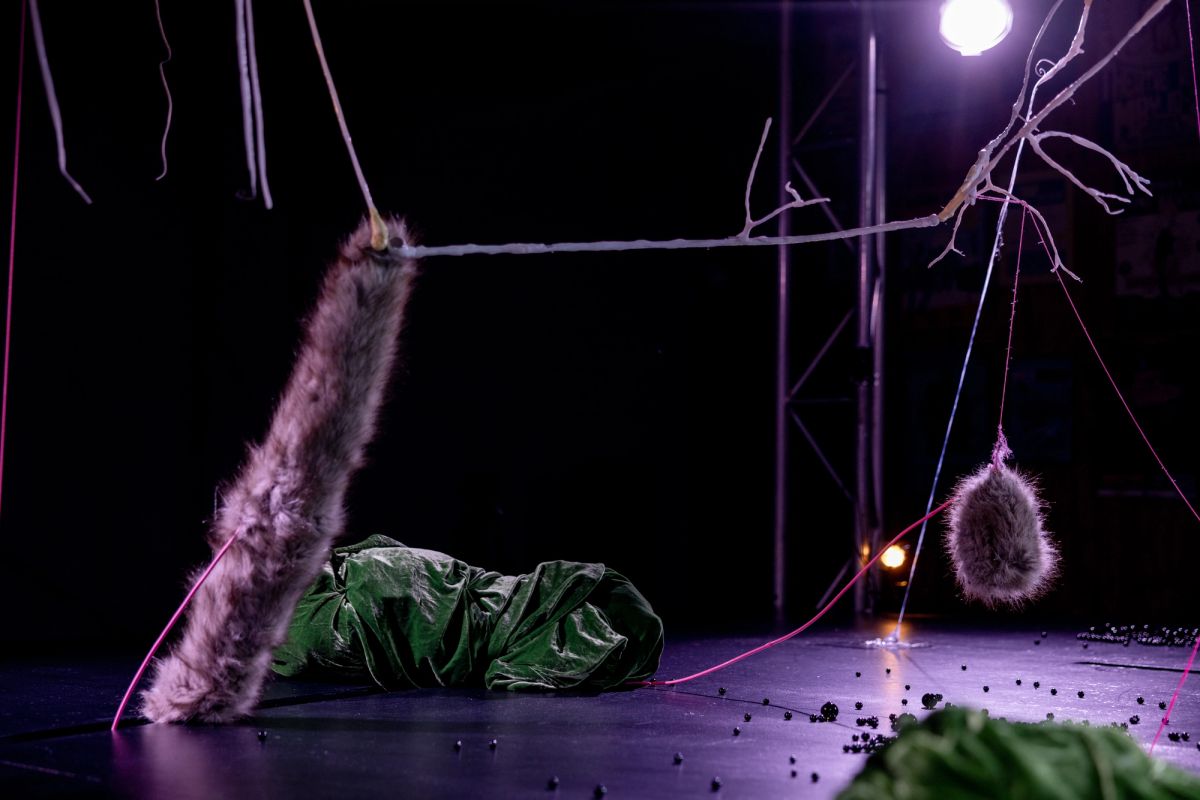 Low-lit stage with oorbeez scattered across the surface, fur elements suspended and resting, and white bone-like structures connected by pink threads.