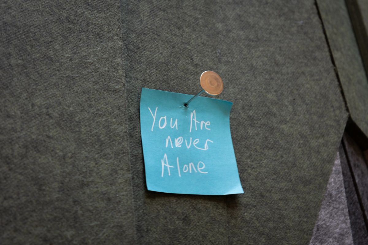 A blue postit note is nailed into a felt mountain, the postit says 'You Are Never Alone'