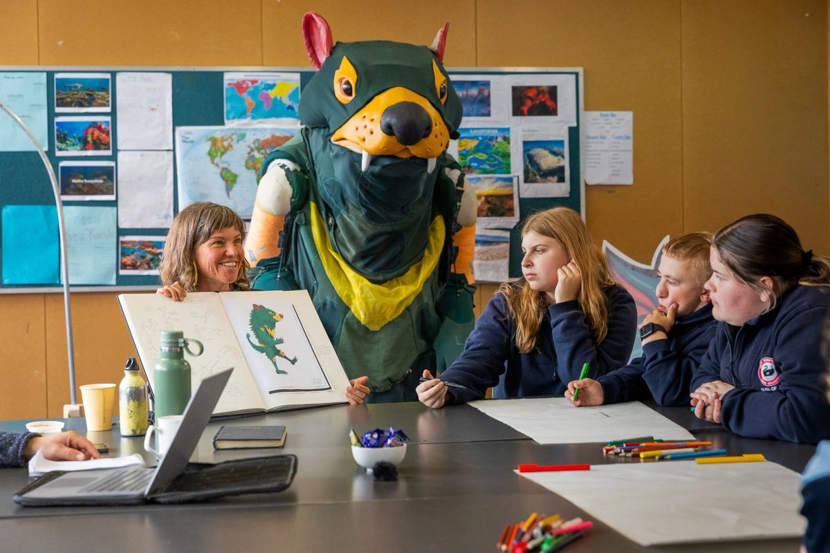 A group of students from New Norfolk High School sit around a table with the designer and maker of the TFC Devil Mascot, Bryony Anderson. Bryony is showing the students her initial designs.