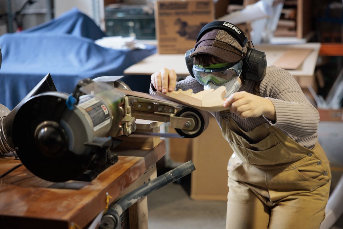 A person in a workshop is grinding or sanding wood on a machine