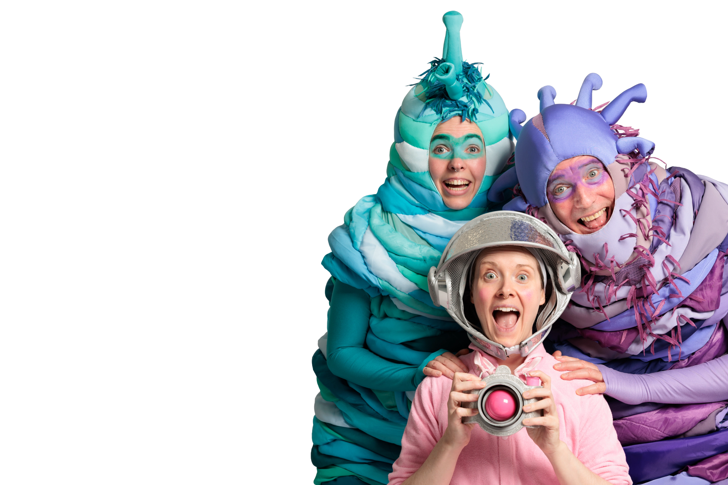 Two alien characters in colourful layered costumes tower behind a delighted child in a pink onesie and space helmet, who holds a camera.