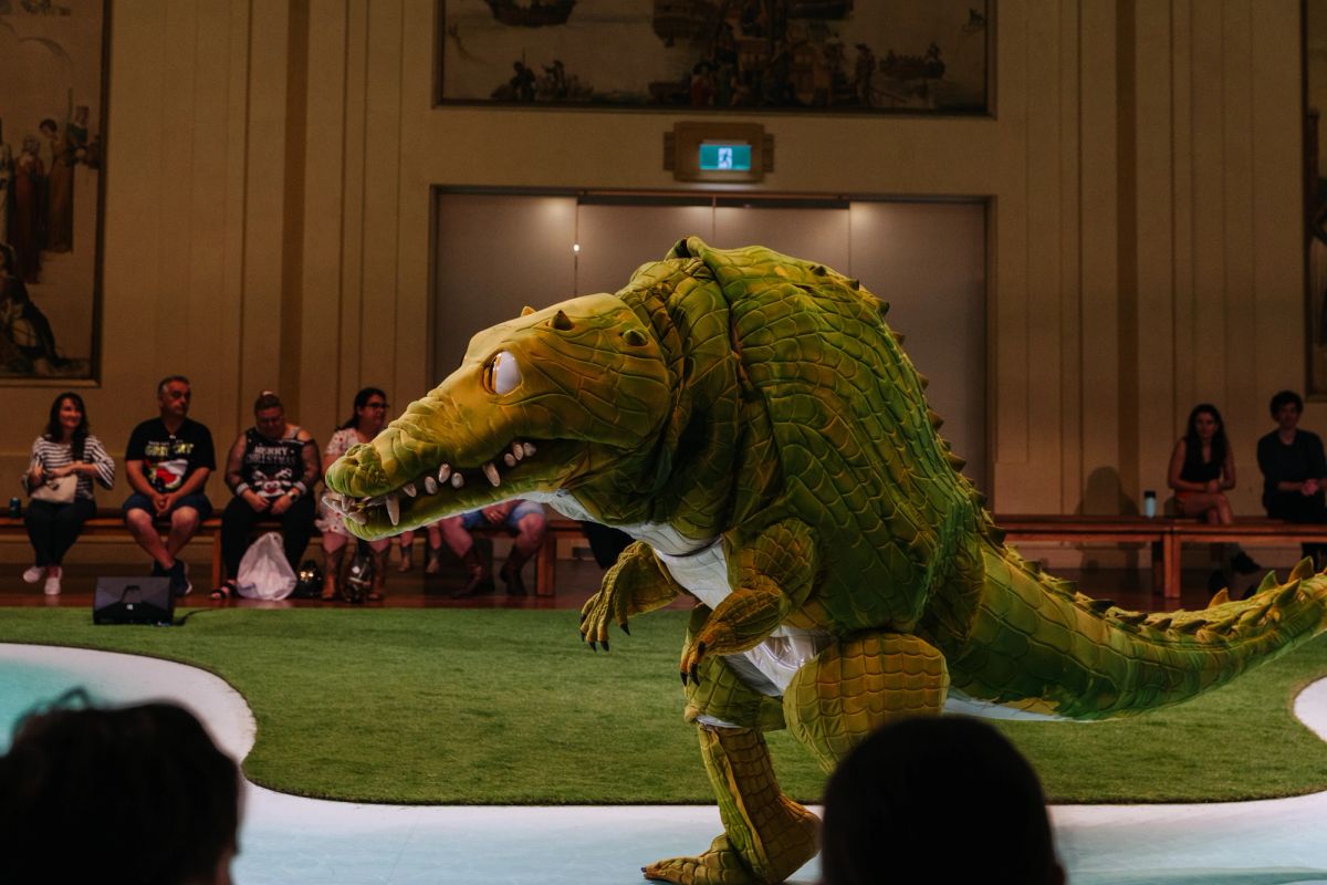 A giant crocodile puppet is walking past a row of people