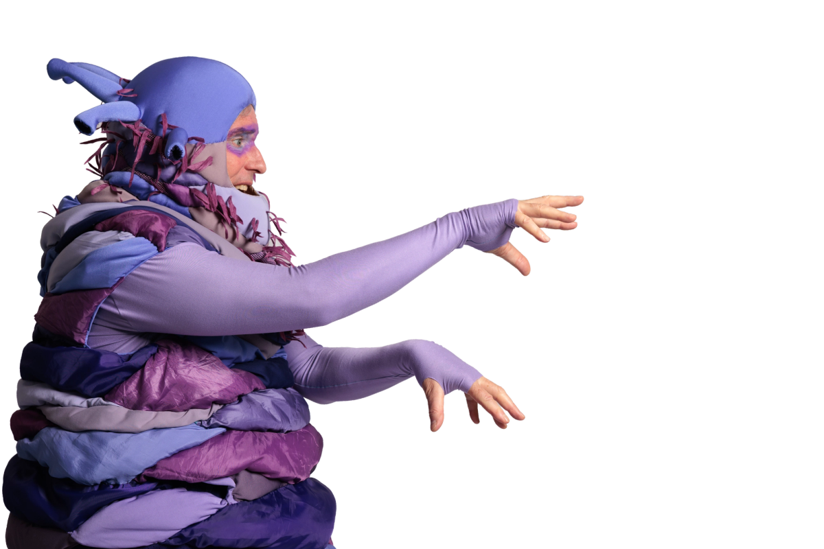 An alien character in a purple and lilac layered costume with antenna-like protrusions reaches both arms forward with hands outstretched, as if grasping or gesturing urgently toward something out of frame.