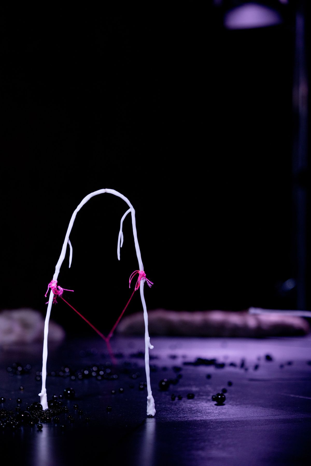 A low-lit stage with oorbeez scattered across the surface and a white, bone-like structure connected by pink threads.