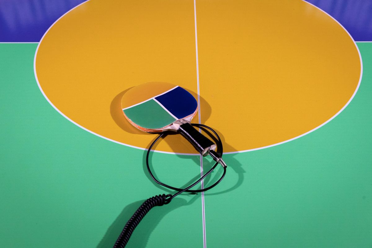 A table tennis bat lays on a green, yellow and blue table