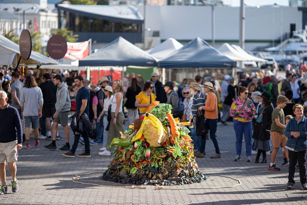 A pile of compost lays on the ground, but this isn't just any compost, it's a performance about to start. Children look on excited. A crowd is surrounding the compost