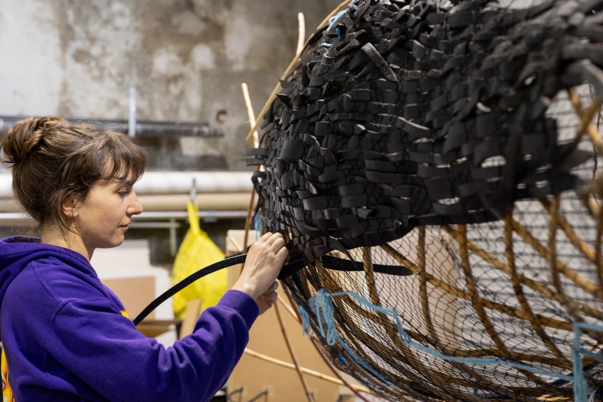 Puppet maker Mads is standing next to a work in progress whale puppet, feeding pieces of black foam through netting to make the skin of the whale