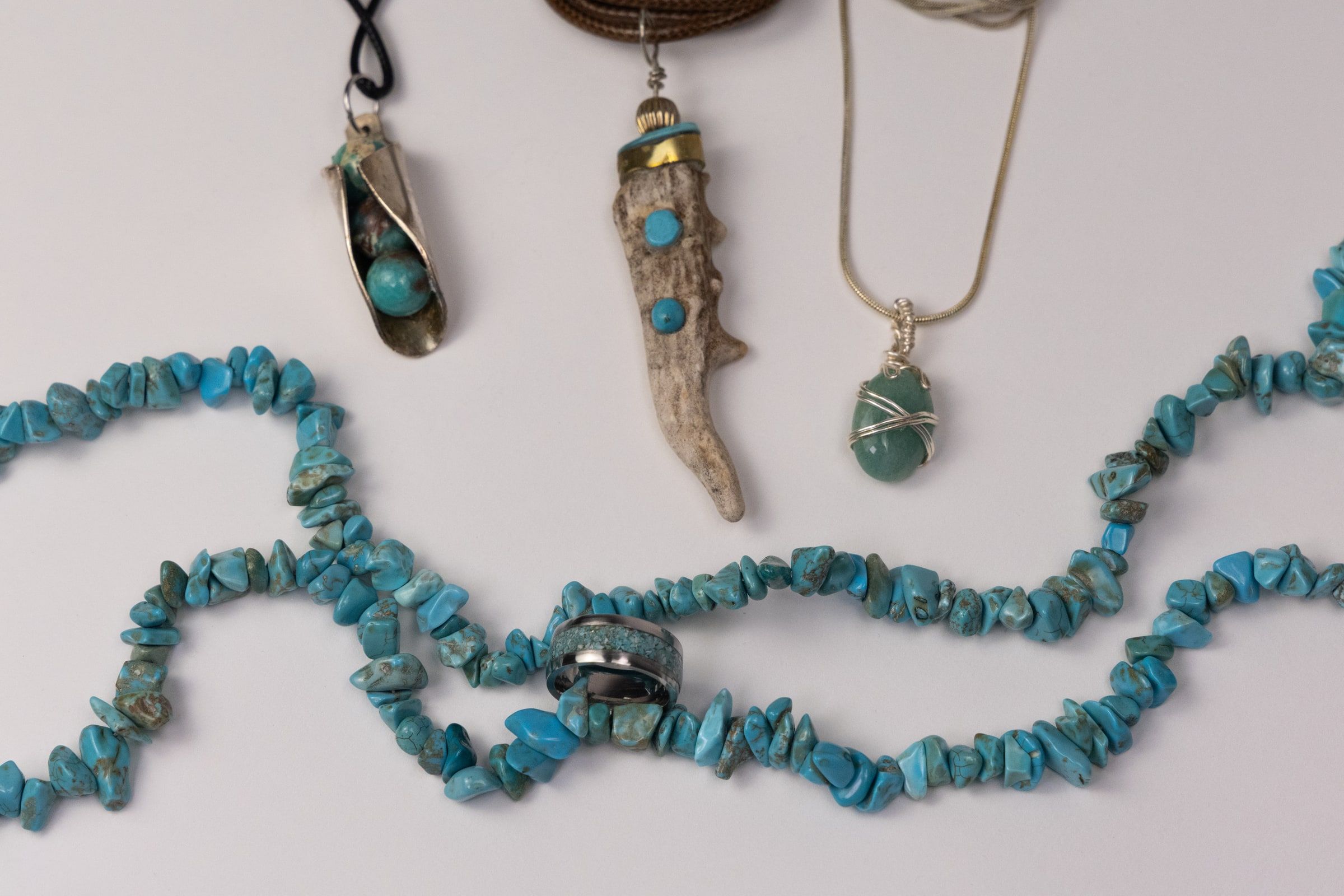 Handmade turquoise jewelry laid out on a white surface, two strands of turquoise chips alongside silver pendants set with turquoise stones.