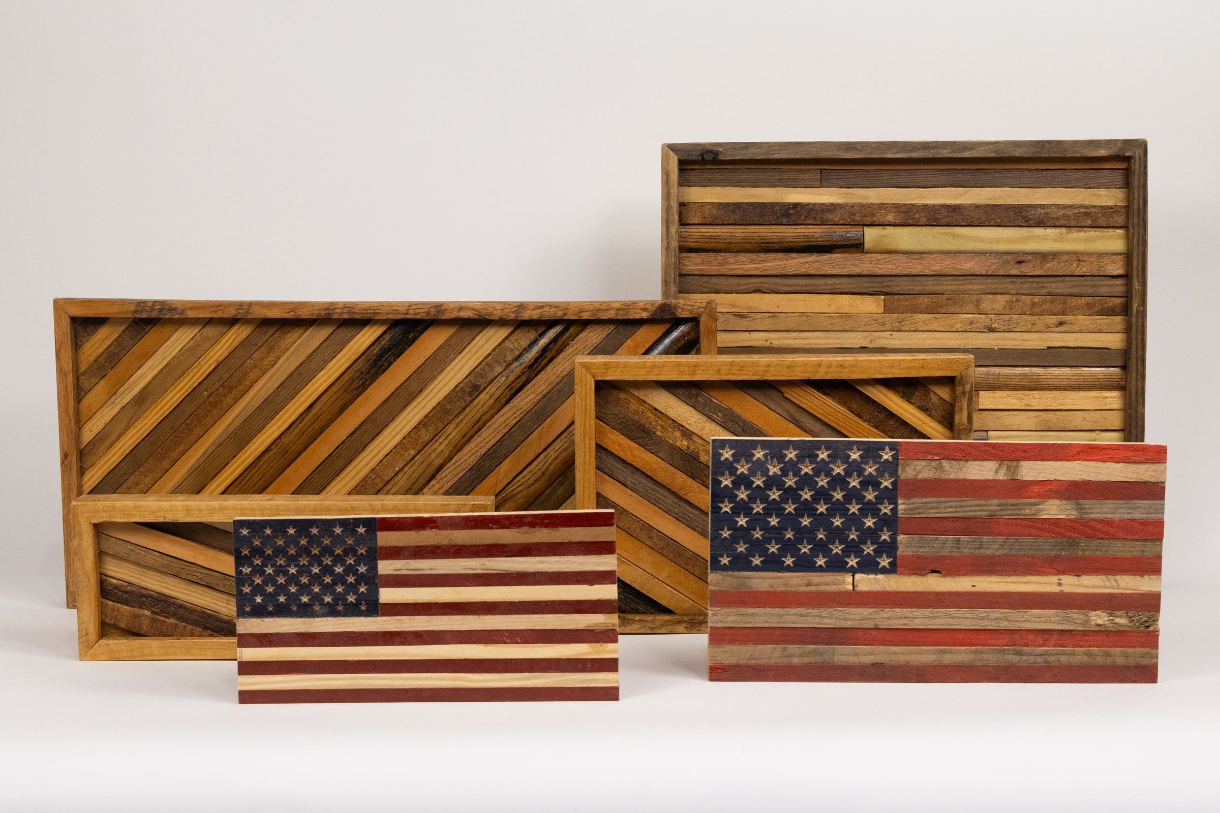 Serving trays and wall pieces built from reclaimed wood, some in diagonal stripes of light and dark grain, others assembled as American flags.