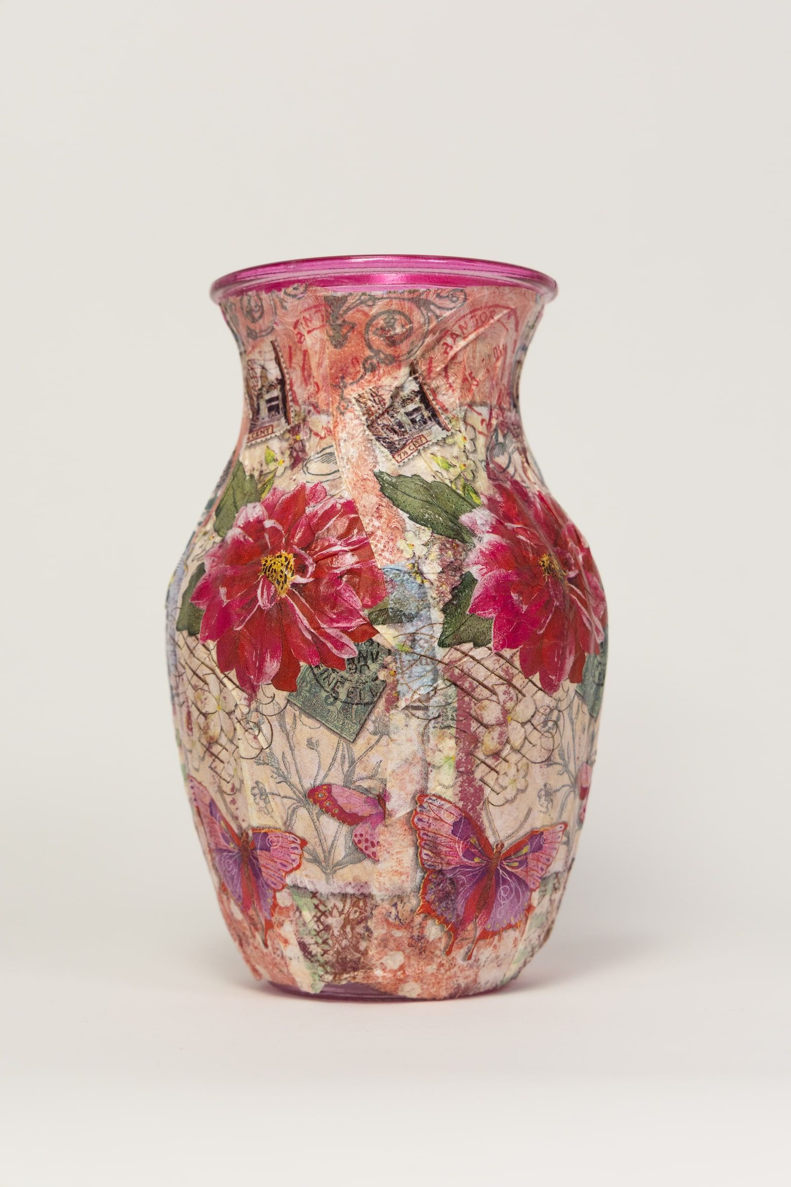 A vase covered in decoupage paper showing large pink and red blooms, finished with a bright pink rim.
