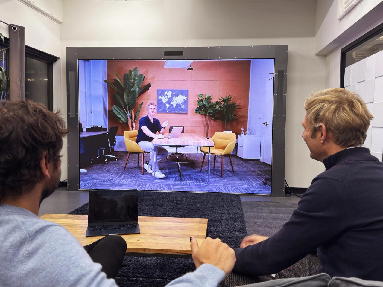 Two colleagues in a Noro room talking with a life-size remote participant on the portal