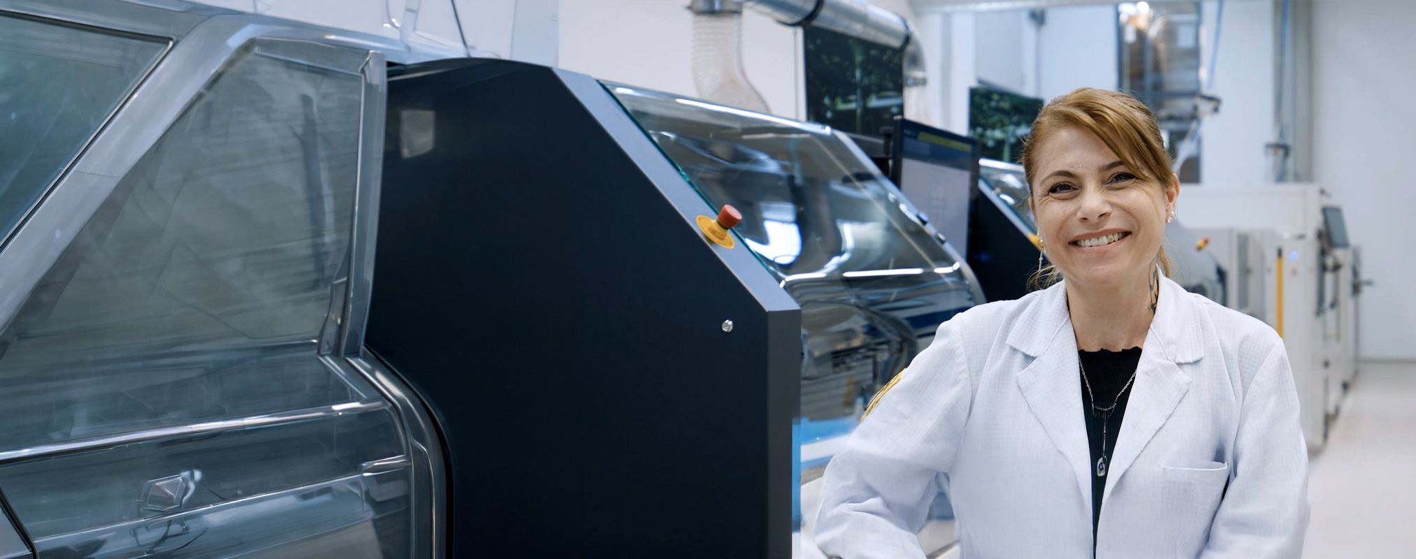 Blonde Frau, lachend, in einer Produktion stehend vor Industriemaschinen
