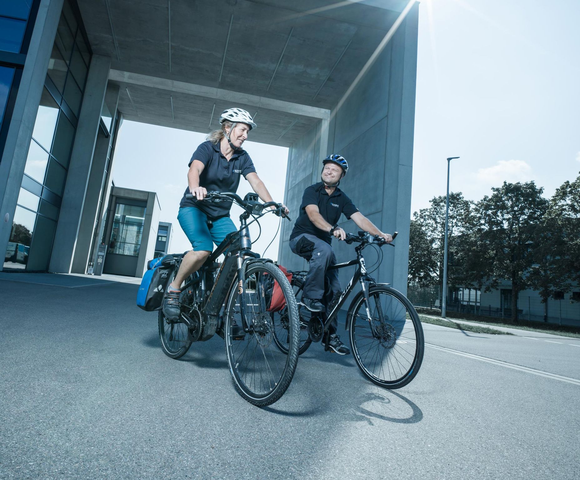 Zwei Mitarbeiterinnen fahren mit dem E-Bike auf dem Firmengelände. Sie haben einen Helm auf. 