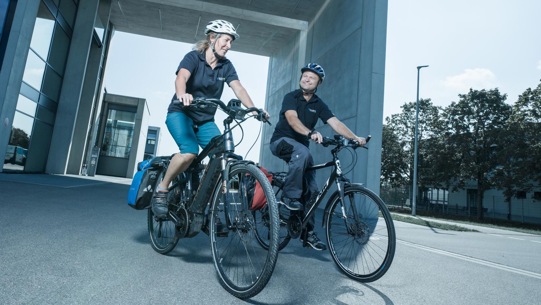 Zwei Mitarbeiterinnen fahren mit dem E-Bike auf dem Firmengelände. Sie haben einen Helm auf.