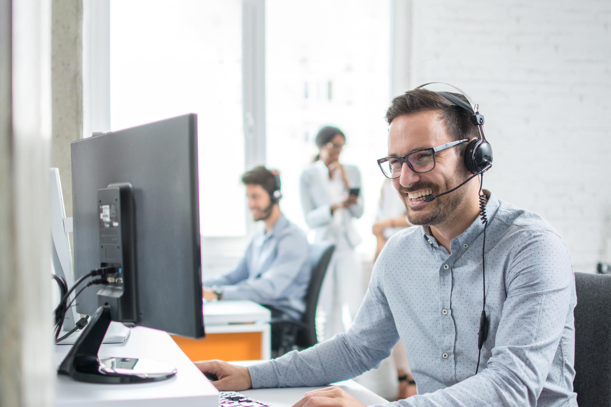 Servicemitarbeiter, der mit einem Headset am rechner sitzt und ein Gespräch führt 