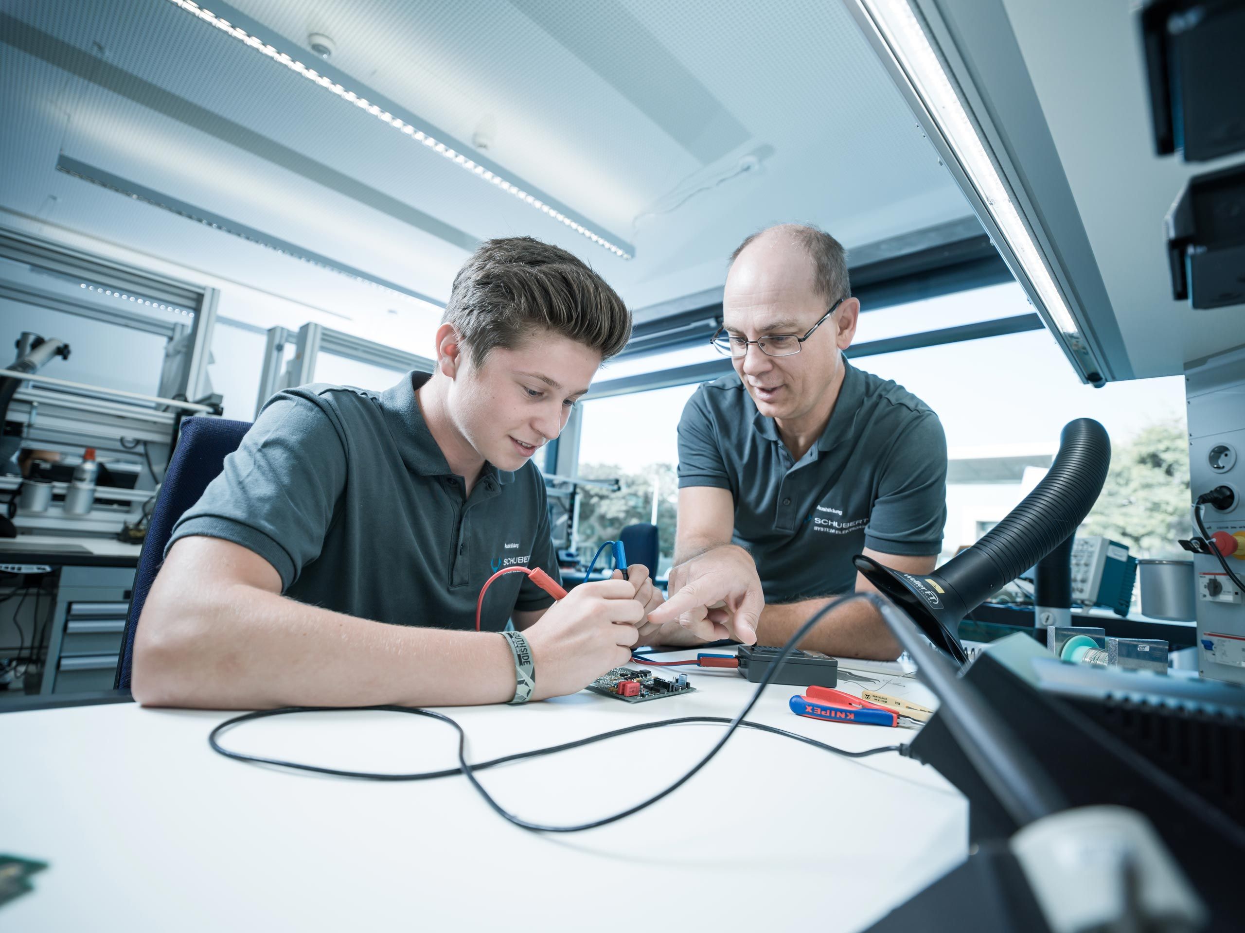 The training manager supports a trainee with soldering 