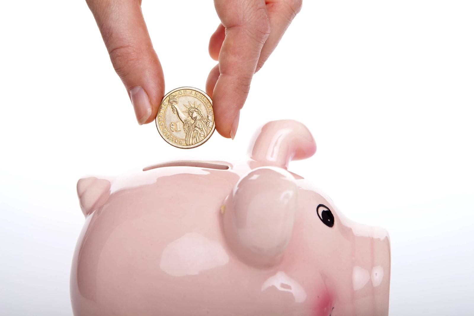 Single coin being put into pink piggy bank.