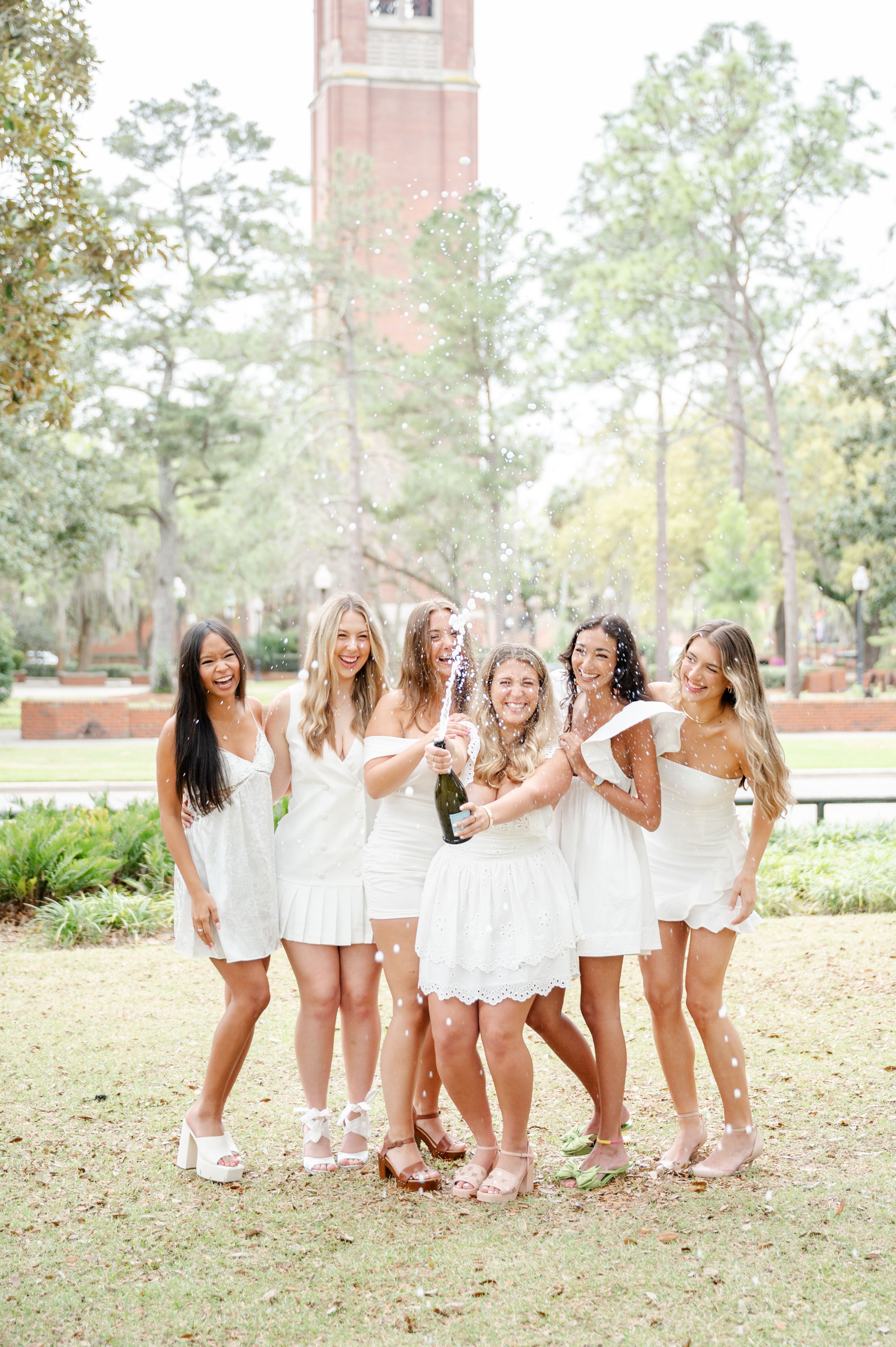 College friends popping champagne to celebrate grad photos in front of Century Tower