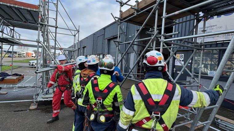Opleiding in het werken op steigers in het Bonapi Training Center; deelnemers met helmen en veiligheidsharnassen tijdens praktische oefeningen op een steigerconstructie