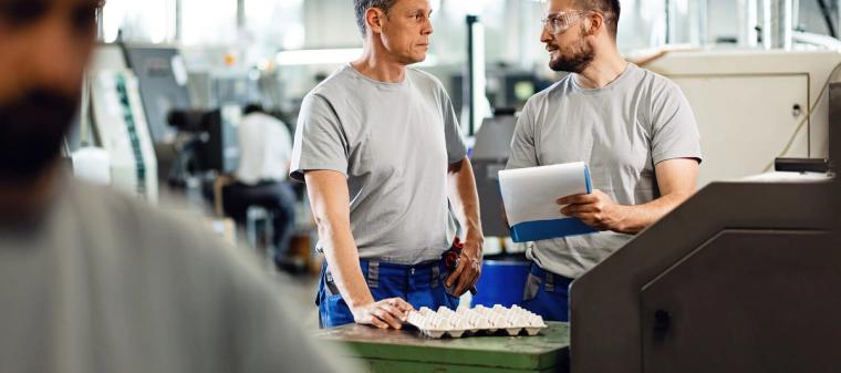 Dwóch pracowników rozmawia przy stanowisku produkcyjnym w hali przemysłowej w Holandii.