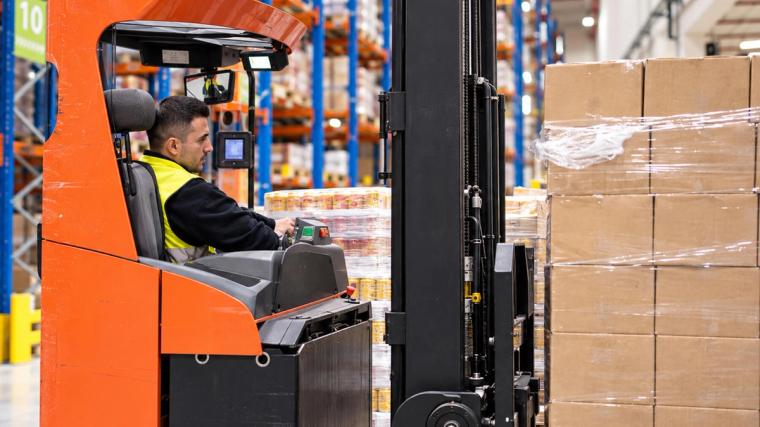 Een bestuurder van een reachtruck tijdens het vervoeren van pallets met goederen in een hoogbouwmagazijn