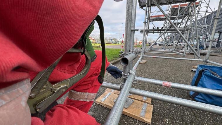 Steigerbouwer tijdens praktische werkzaamheden aan de bouw van een steiger, montage van stalen onderdelen met gebruik van persoonlijke beschermingsmiddelen