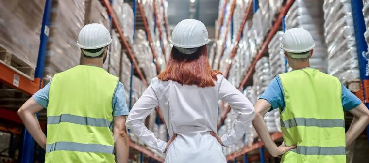 Pracownicy magazynu w kaskach i kamizelkach ochronnych stoją między regałami z towarem w centrum logistycznym w Holandii.
