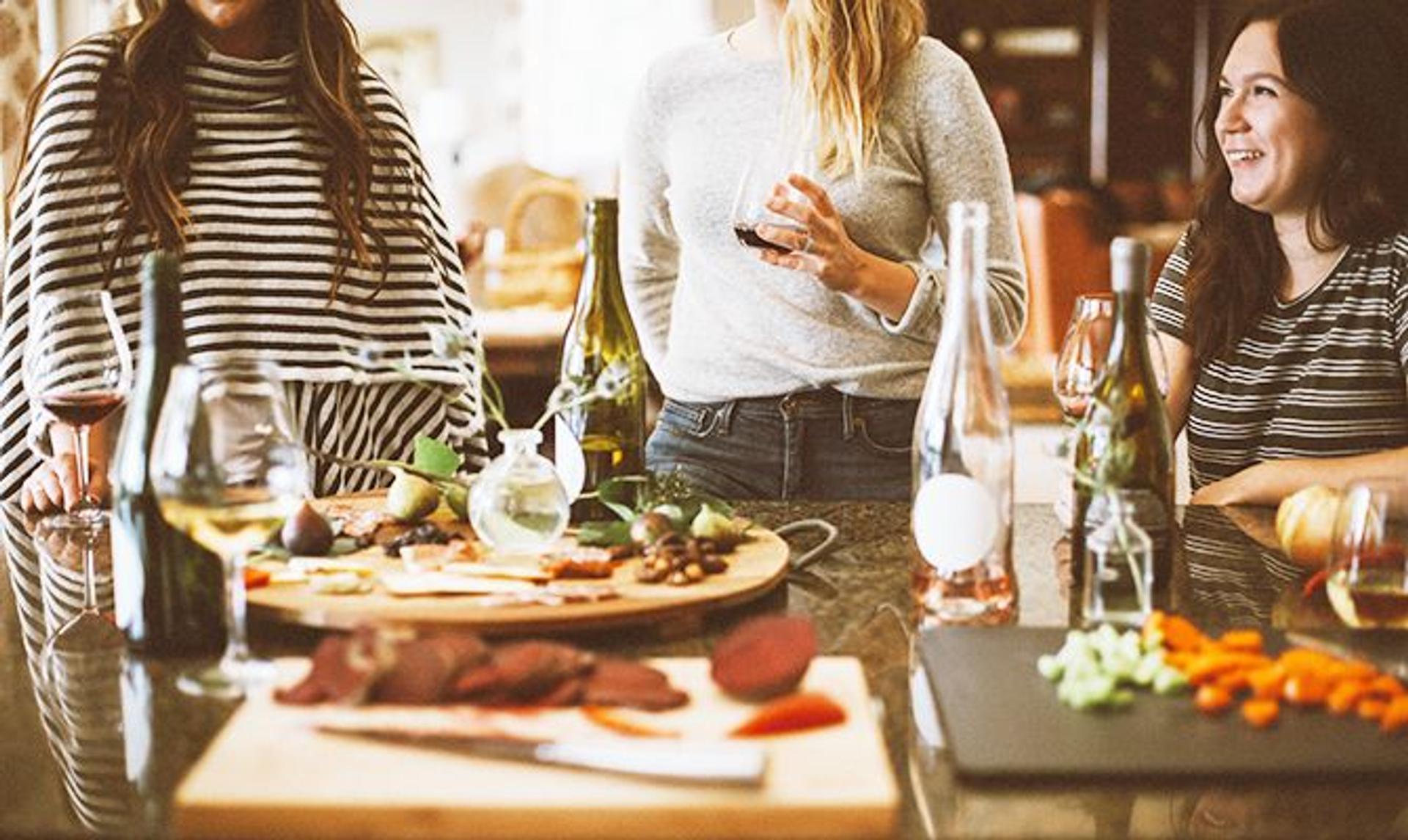 a group of women are sitting at a table eating food and drinking wine .