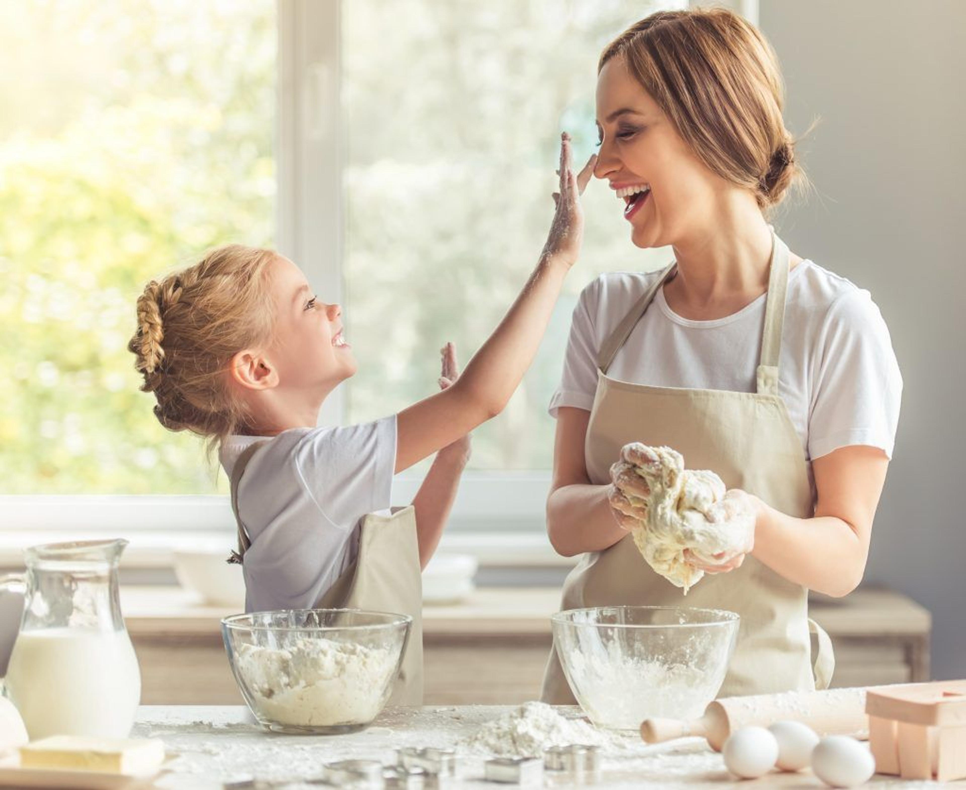 a woman and a little girl are playing with dough in the kitchen .