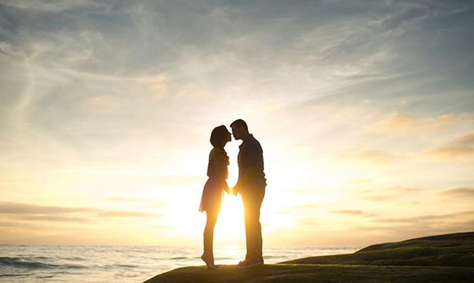 a man and a woman are kissing on the beach at sunset .