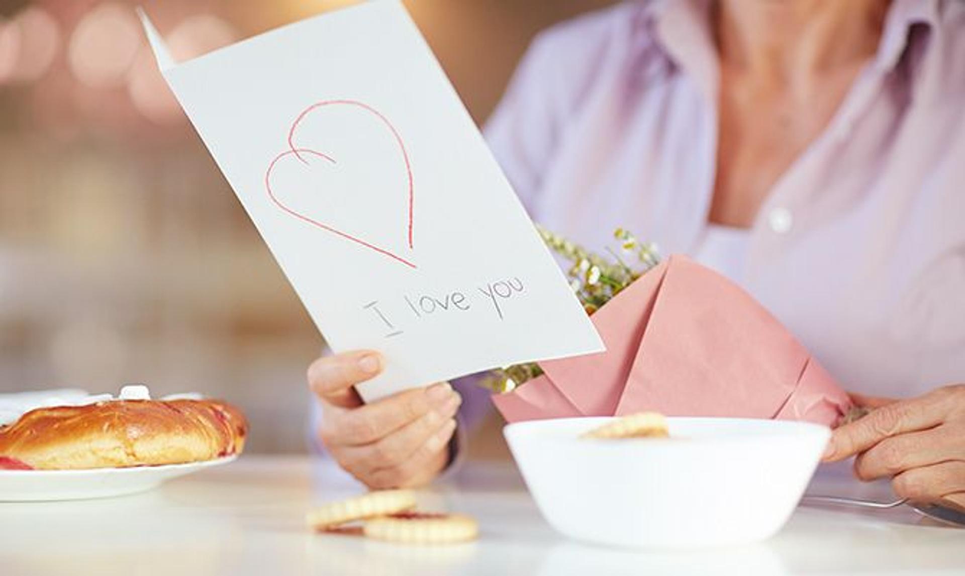 a woman is holding a bouquet of flowers and a card that says `` i love you '' .