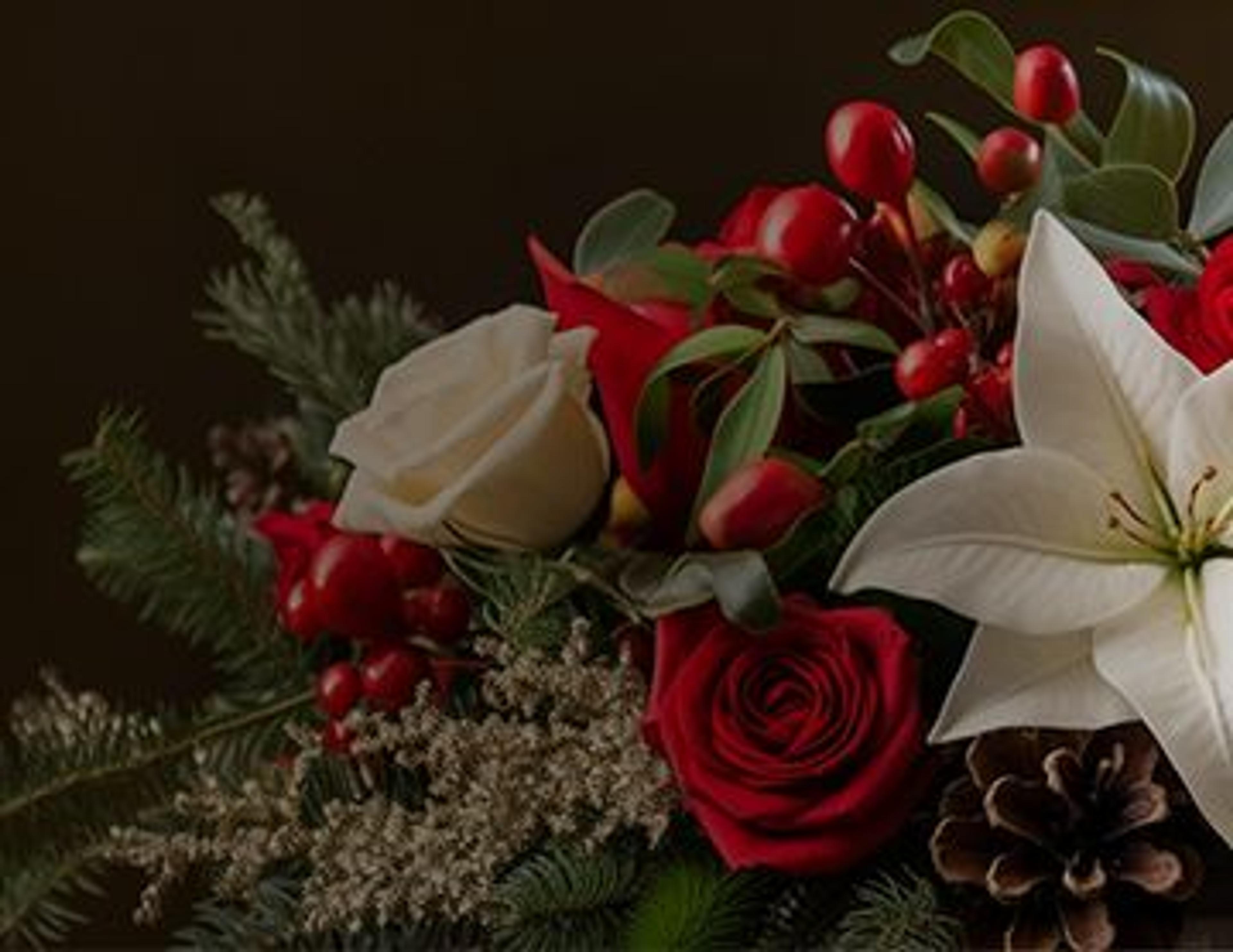 a bouquet of red roses , white lilies , pine cones and berries .