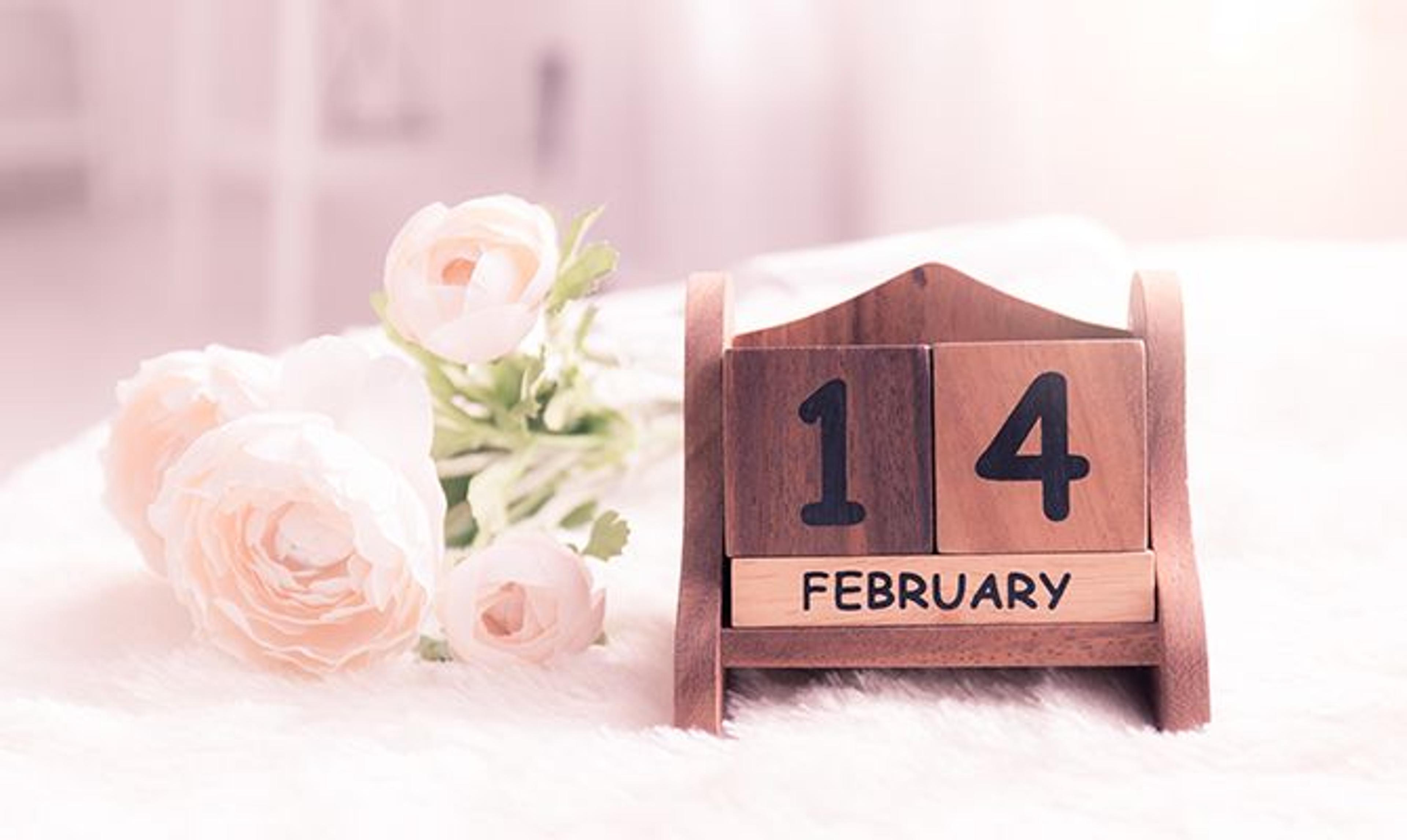 a wooden calendar with the date of february 14 next to a bouquet of flowers .