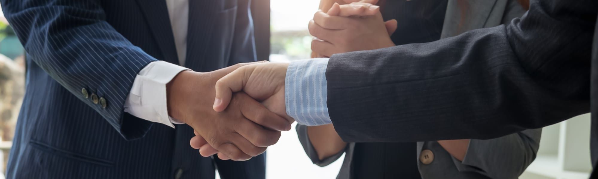 Close-up photo to two corporate businessmen wearing smart suits shaking hands after agreeing a deal. Used to represent blog about strategies for B2B suppliers to secure more market visibility and new customers