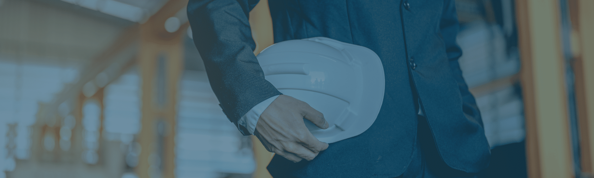 Close up image of a professional holding a hard hat in a warehouse, with a blue tint. Representing the blog titled Cutting costs for a lean supply chain