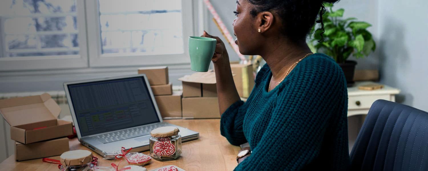 Black female accounting executive with a mug in hand, sat at her desk and looking at her computer. Representing blog titled: VAT Mandates How to ensure your business is eInvoicing ready