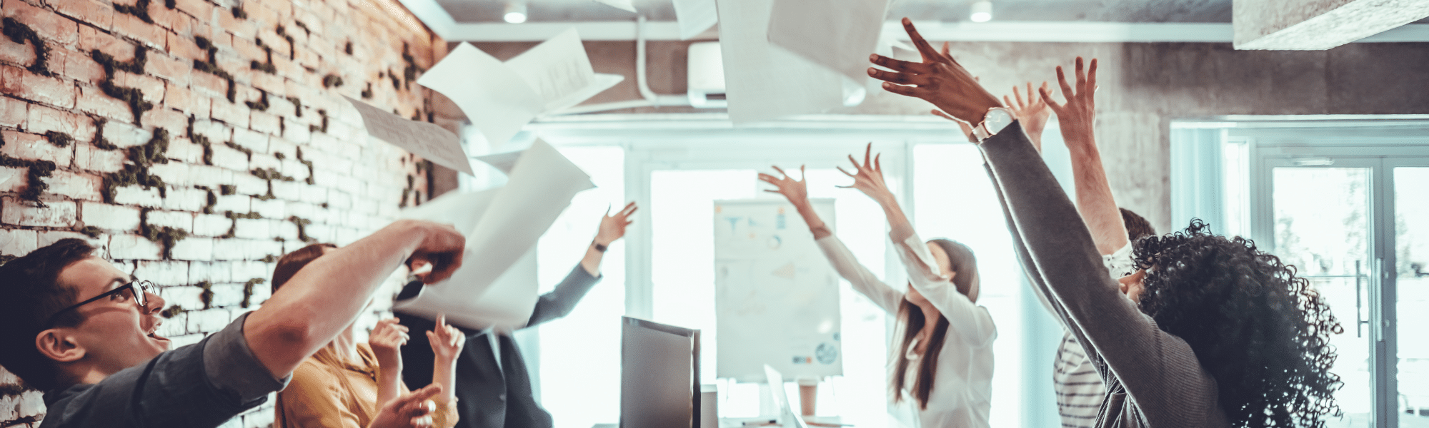 A blog feature image depicts a group of workers in an office, jubilantly throwing sheets of paper in the air. Their celebration signifies the shift from traditional invoicing to the use of eInvoicing through Accounts Receivable automation software.