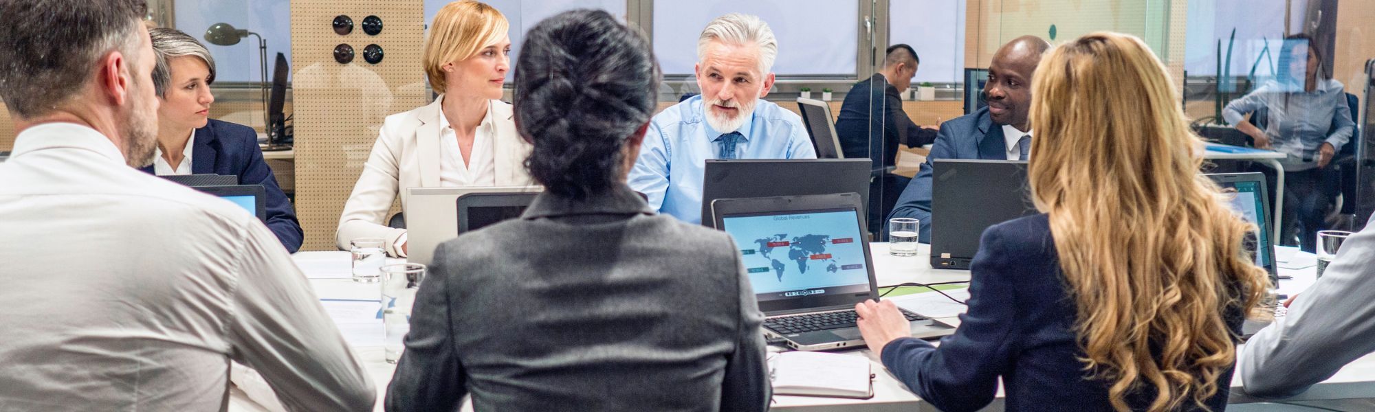 Photo of a corporate board team having a meeting in a board room with laptops. Representing a blog titled "Why CFOs invest in invoice processing"