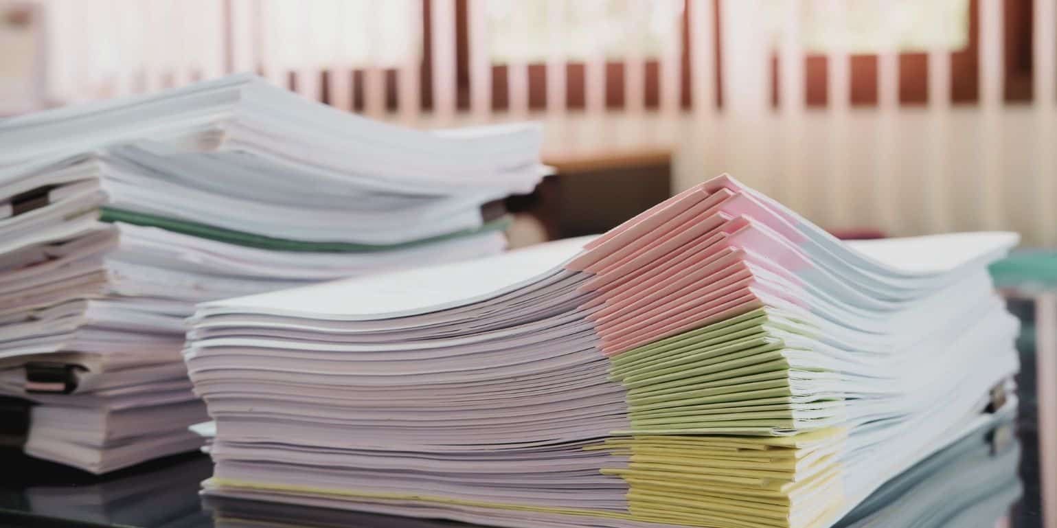 Stock photo close-up of piles of colour coded paper files on an office desk. Representing a blog titled "why switch to electronic invoice processing"