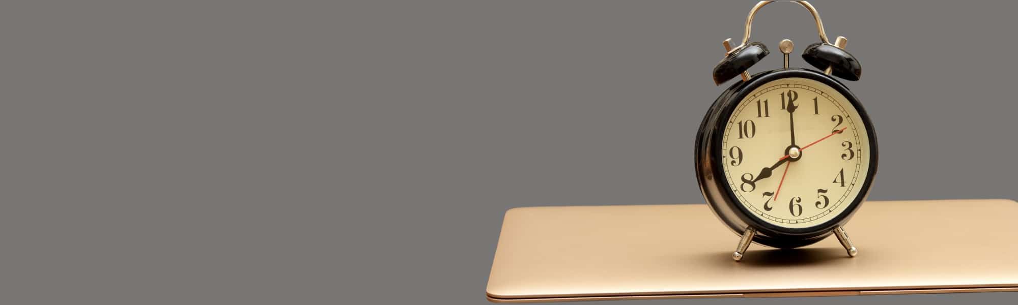 A cutout image of an alarm clock on top of a closed laptop, with a grey background colour. This shows how inefficiency in the finance department can be tackled with Automated accounts payable invoice processing