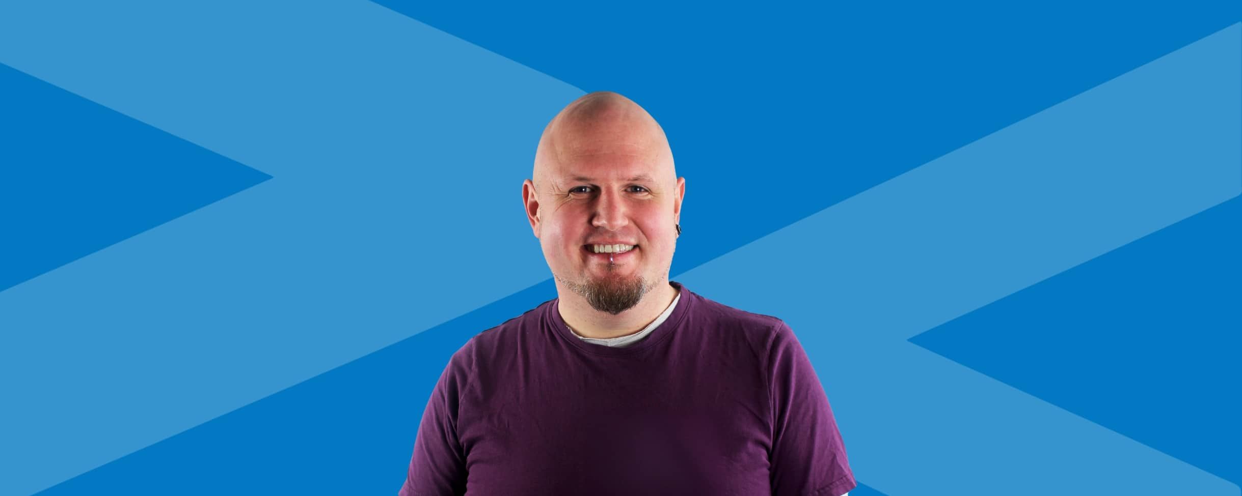 Header image for a Transalis blog focused on the customer support team. Transalis blue background, with brand logo arrows and headshot of Transalis Customer Support Team Manager, Huw Davies