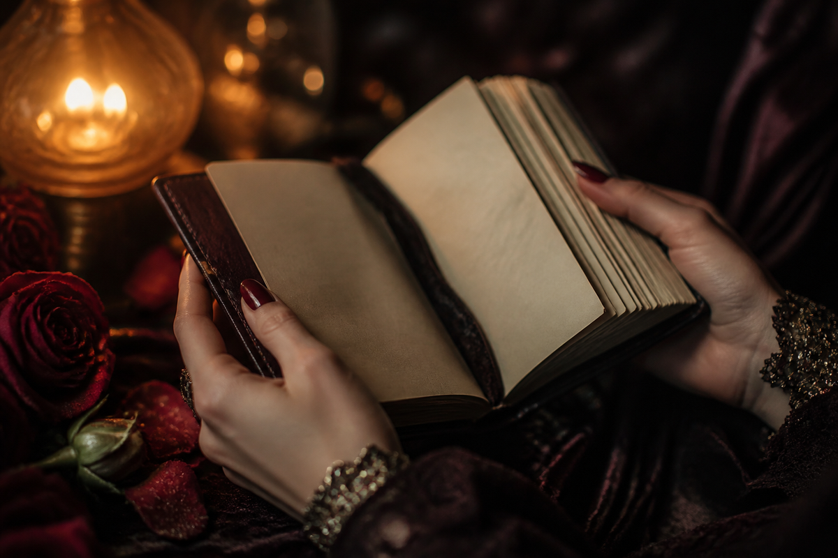 Hands holding an open journal beside roses and amber lamp light