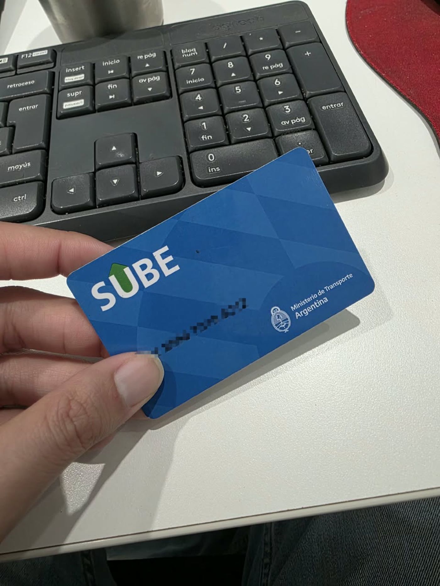 아르헨티나 교통부가 발행한 파란색 SUBE 교통카드를 손으로 든 사진으로, 카드 오른쪽에 아르헨티나 교통부 표기가 인쇄되어 있고 카드 번호는 가려져 있다.
