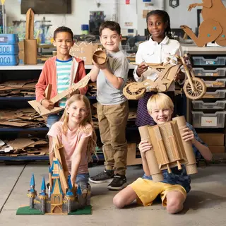 Children holding the cardboard bike, castle and other projects they built with ChompSaw
