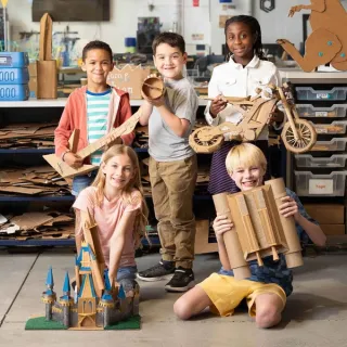 Children holding the cardboard bike, castle and other projects they built with ChompSaw